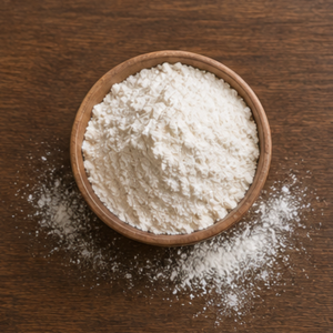 Fine white flour in a wooden bowl on a dark wooden surface, with flour scattered around it